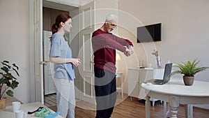 A woman helps an elderly man put on wireless headphones before morning exercises