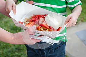 A woman helps her son hold a waffle topped with strawberries and cream purchased from a food truck.