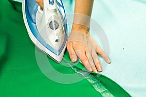 Woman hemming, shortening green courtain fabric with an adhesive iron-on hemming tape photo