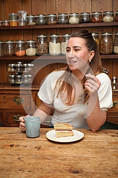 A woman in her 30`s chatting with a mug of coffee and a slice of cake