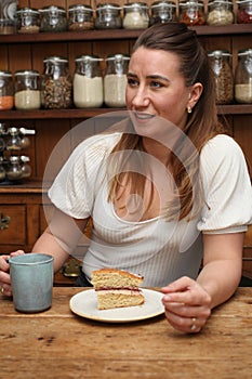 A woman in her 30`s with a coffee and a slice of cake in her country kitchen