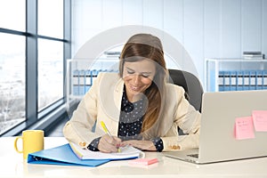 Woman on her 30s at office working at laptop computer desk taking notes