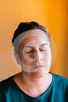 Woman in her 50s with brown hair pulled back, serious, sad and pensive with her eyes closed