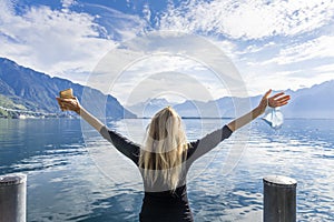 Woman with her arms raised gesturing freedom with a mobile phone and a mask in front of a lake