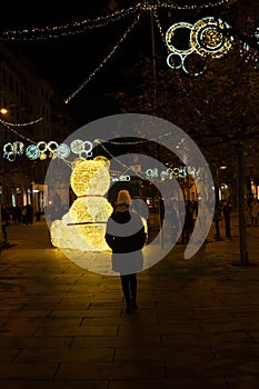 woman with her back turned looks at a large bear illuminated with light bulbs at Christmas time