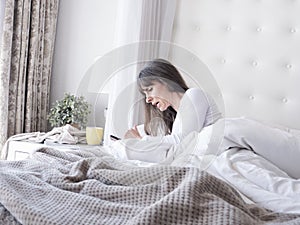 Woman on her bed with mobile phone and coffee