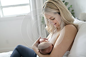 Woman in her bedroom on the white cushions, smiling and breastfeed her baby.