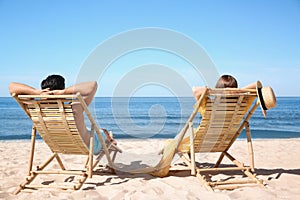 Woman and her boyfriend on deck chairs at beach. Lovely couple