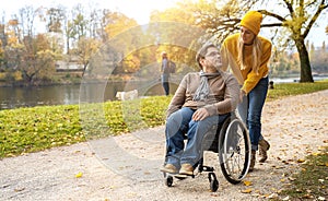 Woman and her boyfriend in a wheelchair having stroll through the park at a river enjoying a autumn day