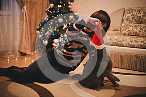 Woman with her cat wearing Santa Claus hat near christmas tree