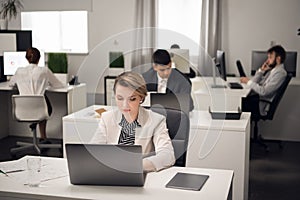 Woman and her collegues sit at a table with laptop