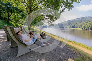 Woman with her dachshund taking a break, lying on large bench, banks of the Prum river