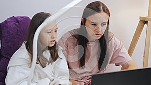 A woman and her daughter do homework together in front of a laptop or study remotely.