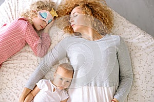 Woman and her daughter having rest on the bed while the baby has waken up