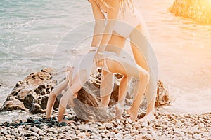 Woman and her daughter practicing balancing yoga pose on one leg up together on rock in the sea. Silhouette mother and