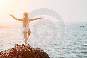 Woman and her daughter practicing balancing yoga pose on one leg up together on rock in the sea. Silhouette mother and