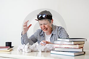 woman at her desk with books and crumpled sheets of paper. Creative crisis, learning difficulties