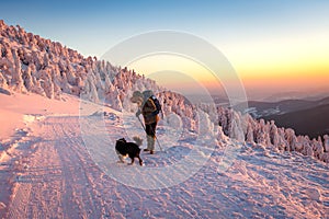 Woman with her dog hiking in winter mountain during sunset