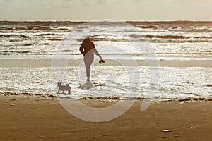 Woman and her dog walking at the beach at sunset or sunrise