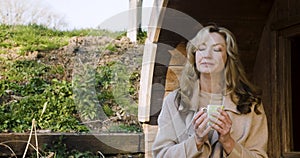 Woman in her forties outside thoughtful, sad or depressed in golden winter sunshine drinking mug of coffee or cup of tea