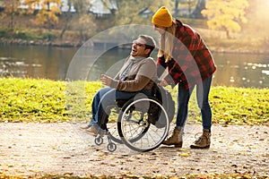 Woman and her friend in a wheelchair having stroll through the park at a river enjoying the autumn