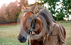 A woman and her horse in rural surroundings, on a grassy field. Portrait of a young equestrian amid nature, training horses, and