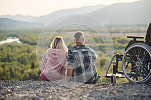 Pretty woman and her incapacitated husband resting together near his wheelchair on the hill. photo