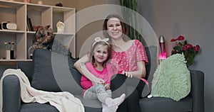 Woman and her little daughter sitting on the sofa and watching comedy film on TV and laughing