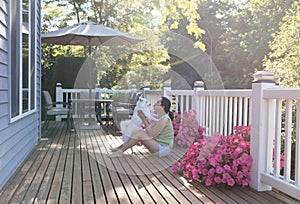 Woman and her pet dog outdoors on home deck during bright sunlight on a lovely summer morning