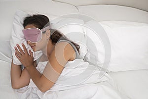 woman in her sleep mask sleeps beneath a comforting blanket, a testament to healthy sleep habits.