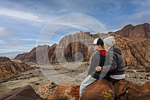 Woman and her son sitting on a rock ledge overlooking beautiful Snow Canyon State park in the deserts of Utah