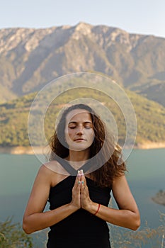 Woman in her thirties, hands in namaste with eyes closed in front of the mountains