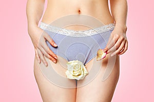 A woman in her underwear holds a white rose flower between her legs and a withered petal in her hand. Close up. Pink background.