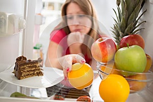 Woman hesitating whether to eat cake or orange