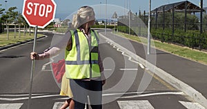 Woman with Hi-vest holding stop sign while girl riding scooter and crossing the road