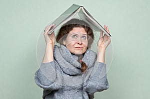 A woman hides under a book, as if under a roof from hostile factors: stress, depression, fear