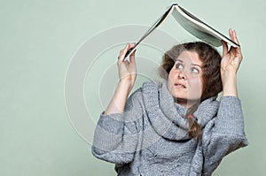 A woman hides under a book, as if under a roof from hostile factors: stress, depression, fear