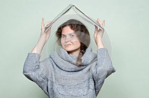 A woman hides under a book, as if under a roof from hostile factors: stress, depression, fear