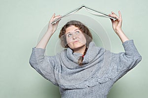 A woman hides under a book, as if under a roof from hostile factors: stress, depression, fear