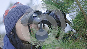 Woman hiding behind pine tree and using binoculars