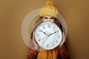 Woman hiding behind round clock remind about autumn time change