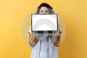 Woman hiding half of her face behind laptop with empty display, mockup, copy space for promotion.