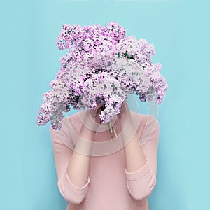 Woman hiding head in bouquet lilac flowers over colorful blue