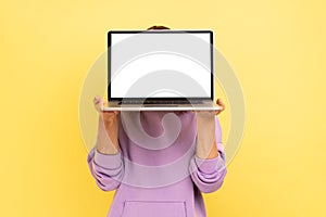 Woman hiding her face behind laptop with blank display for advertisement or promotional text.