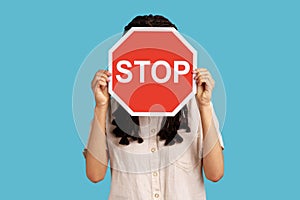 Woman hiding her face behind red stop traffic symbol, warning, avoids forbidden actions.