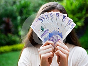 Woman hiding her face with a range of fifthy tousand pesos bill and garden