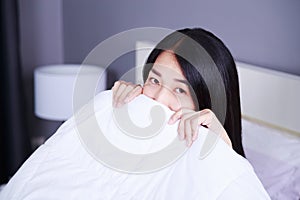 Woman hiding under a blanket on bed in bedroom