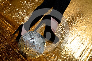 Woman in a high heel shoes standing on a disco ball on a glitter gold background