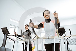 woman with hijab exercising with friend on static elliptical cycle machine