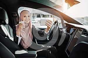 Woman in hijab having video call on mobile inside car